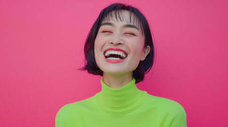 Exuberant Joy: Asian Woman Laughing with Eye-Catching Green Top on Pink Backgroundの素材