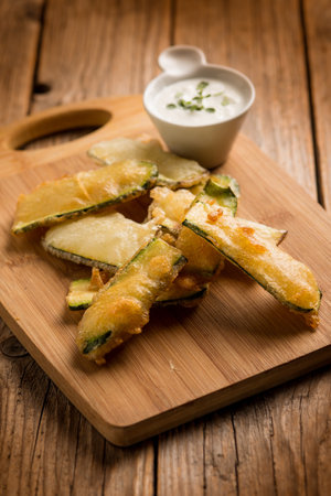 tempura zucchini with sauce over wood boardの写真素材
