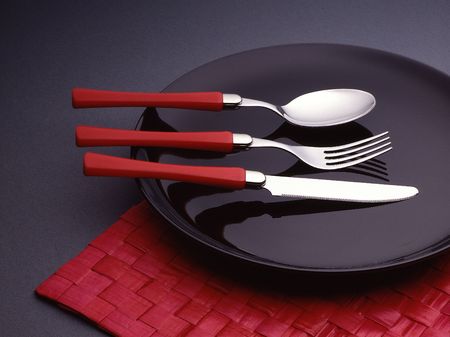 Spoon, fork and knife on a black plate.