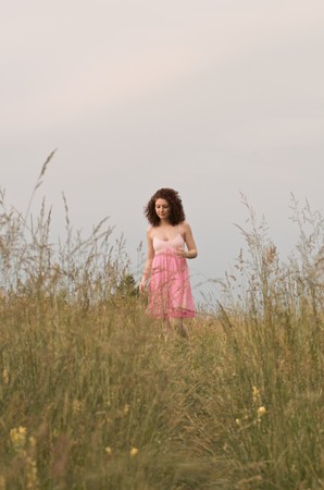 A young woman wearing a pink dress is smiling and standing in a field. Vertical shot.の写真素材
