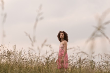 A young woman wearing a pink dress is standing in a field. Horizontal shot.の写真素材