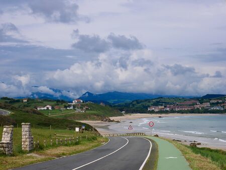 downhill road with mountains in the background and dark seaの写真素材