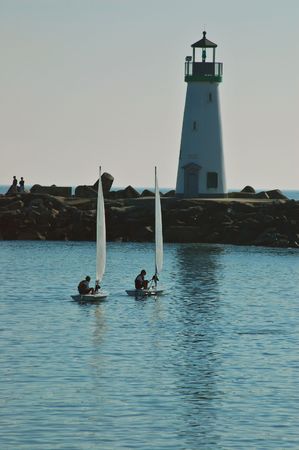 a couple of sail dinghies out in the ocean by the lighthouseの写真素材
