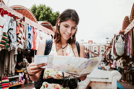 hispanic woman backpacker holding a map in a traditional mexican Market in Mexico, Vacations
