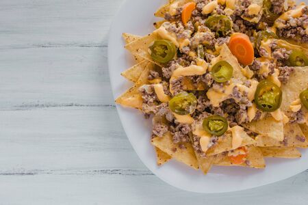 nacho chips corn garnished with ground beef, melted cheese, chili peppers in plate on wooden table mexican spicy food in mexicoの写真素材