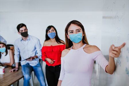 Latin woman teamwork working in business office wearing face mask for social distancing in new normal situation protecting and preventing the infection of covid-19, mexican coworkers in Mexicoの写真素材