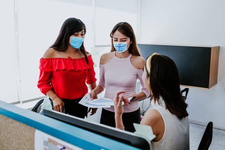 Mexican women working in business office and wearing medical face mask for social distancing in new normal situation protecting and preventing the infection of covid-19, mexican coworkers in Mexico cityの写真素材