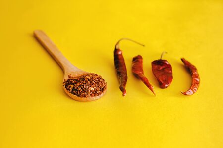 Dried red chili peppers and chili powder spice on yellow background