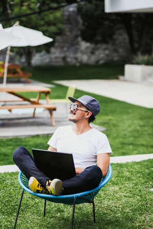 Latin Man working with laptop outdoor in a beautiful terrace using smartphone and computer sitting...