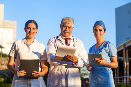 Latin team of medical doctors are looking at camera and smiling while standing outside of mexican...