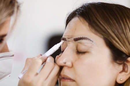 Latin Cosmetologist preparing to mexican woman for eyebrow permanent makeup procedure in Mexico,...