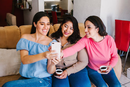 Latin women friends taking a selfie photo and drinking coffee in home in Mexico city