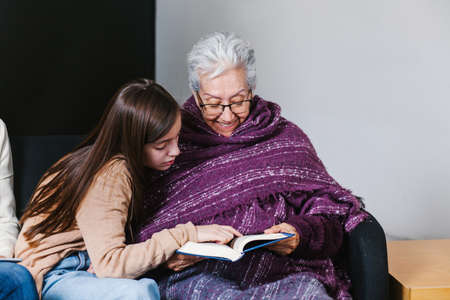 Latin granddaughter and mexican grandmother reading a book and tablet in Mexico cityの写真素材