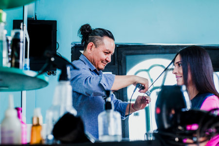 latin man working as a hairdresser and cutting hair of a female customer in a beauty salon small business in Mexico cityの写真素材