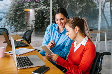 Young latin woman in wheelchair working with computer at workplace or office in Mexico city