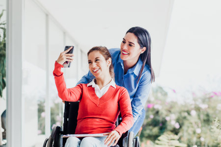 Young latin woman in wheelchair taking a selfie photo at workplace with another woman in Mexico