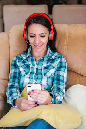 latin woman listening to music and keeping eyes closed while sitting on sofa at home in Mexicoの写真素材