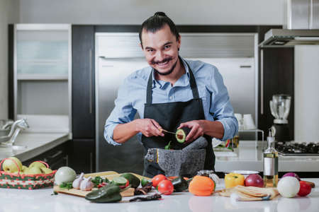 latin man cooking at home preparing salad or mexican sauce in kitchen at home in Mexico cityの写真素材
