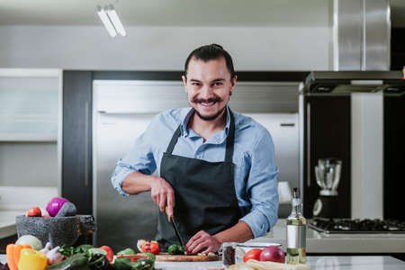 latin man cooking at home preparing salad or mexican sauce in kitchen at home in Mexico cityの写真素材