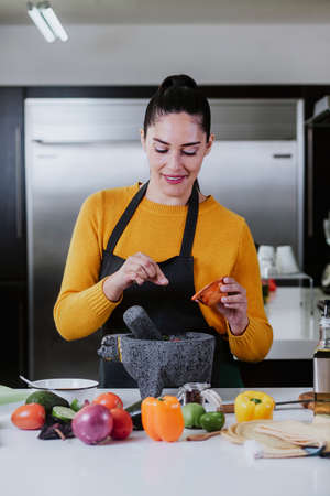 latin woman cooking mexican sauce food in kitchen at home in Mexico cityの写真素材
