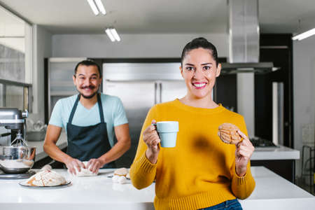 latin couple bakers cooking and eating mexican bread called Conchas with hot chocolate at kitchen in Mexico cityの写真素材
