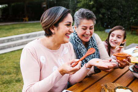 latin grandmother and granddaughter, daughter cooking mexican food at home, three generations of women in Mexicoの写真素材