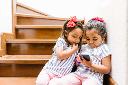 latin child or little girls with phone and tablet at home in Mexico cityの写真素材