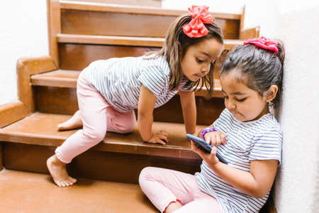 latin child or little girls with phone and tablet at home in Mexico cityの写真素材