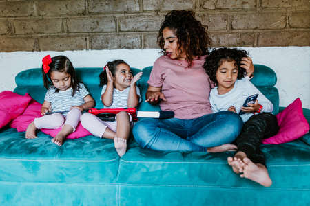 Young latin woman and her little children reading books at home in Mexico cityの写真素材
