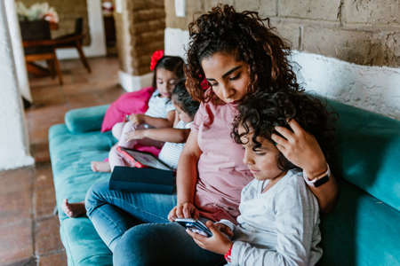 latin mother on sofa at home with little boy child use phone browse Internet together in Mexico cityの写真素材