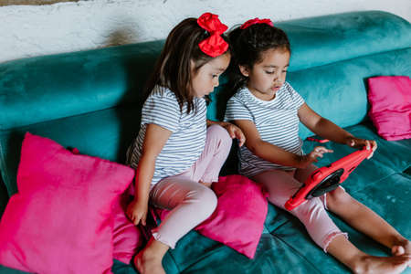 latin child or little girls with phone and tablet at home in Mexico cityの写真素材