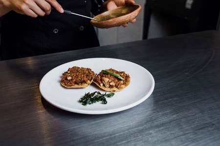 Latin woman chef cooking tostadas of Bacalao a la Vizcaina traditional Mexican food in a restaurant...