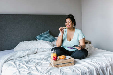 Young latin woman having breakfast in her room in Latin Americaの写真素材