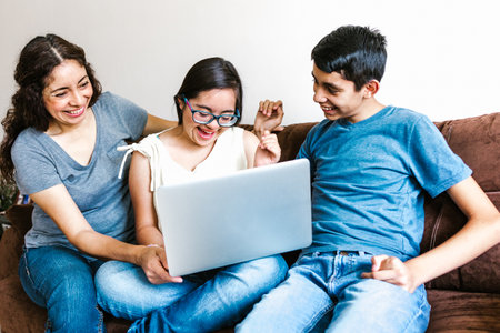 Mexican family and teenage daughter with down syndrome sitting on the sofa with computer at home, in disability concept in Latin Americaの写真素材