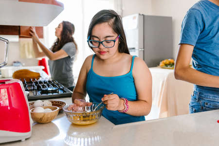 Mexican teenage girl with down syndrome with her family cooking in the kitchen at home, in disability concept in Latin Americaの写真素材