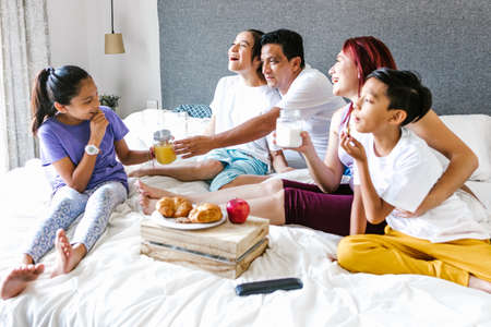 Latin family and teenage daughter with cerebral palsy enjoying breakfast in the bedroom, in disability concept in Latin Americaの写真素材