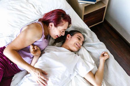 Hispanic teen girl with cerebral palsy lying in bed with her mother smiling, in disability concept in Latin Americaの写真素材