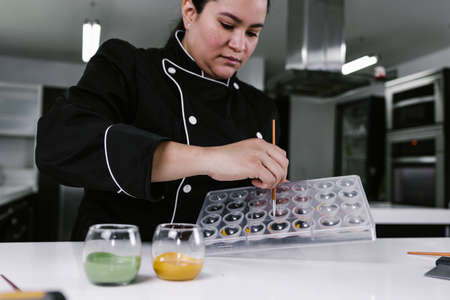 latin woman pastry chef wearing black uniform in process of preparing delicious sweets chocolates at kitchen in Mexico Latin Americaの写真素材