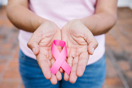 woman hands holding pink breast cancer awareness ribbons with blue sky as background in Latin...