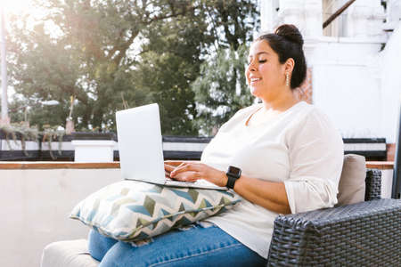 Chubby latin girl working on computer sitting on terrace in Latin America