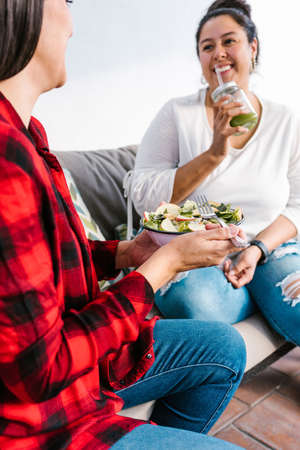 Young hispanic female eating salad and drinking green juice at home in Latin Americaの写真素材
