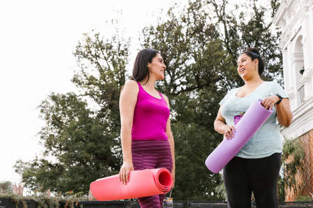 Young latin women chatting while holding a yoga mat outdoors in Mexicoの写真素材