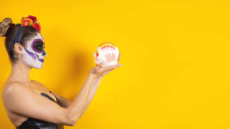 Mexican Catrina, portrait of young latin woman holding a sugar calaverita or sweet skeleton for Halloween party in Mexicoの写真素材