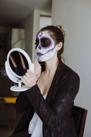 Mexican Catrina, young latin woman putting on makeup her self and making a traditional skeleton for Day of the Dead or Halloween in Mexicoの写真素材