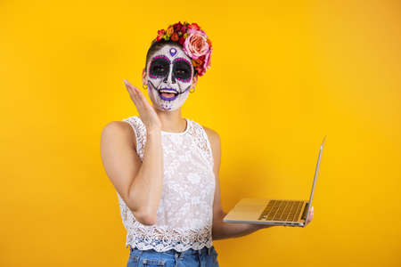 Mexican Catrina, portrait of young latin woman holding computer or laptop, Halloween party in Mexicoの写真素材