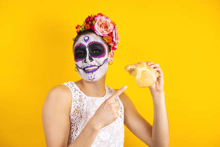 Mexican Catrina, portrait of young latin woman holding mexican hojaldra traditional bread, Halloween party in Mexicoの写真素材