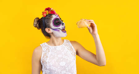 Mexican Catrina, portrait of young latin woman holding mexican hojaldra traditional bread, Halloween party in Mexicoの写真素材