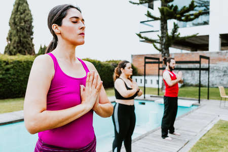 Middle aged hispanic woman standing meditating with eyes closed in group yoga session in Latin Americaの写真素材