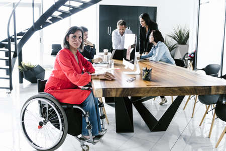Latin transgender woman in wheelchair participating in business meeting with team in conference room in Mexico Cityの写真素材