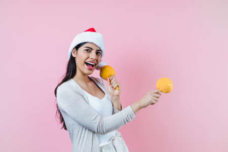 Portrait of young latin woman holding maracas rattle with copy space in a christmas concept on pink...